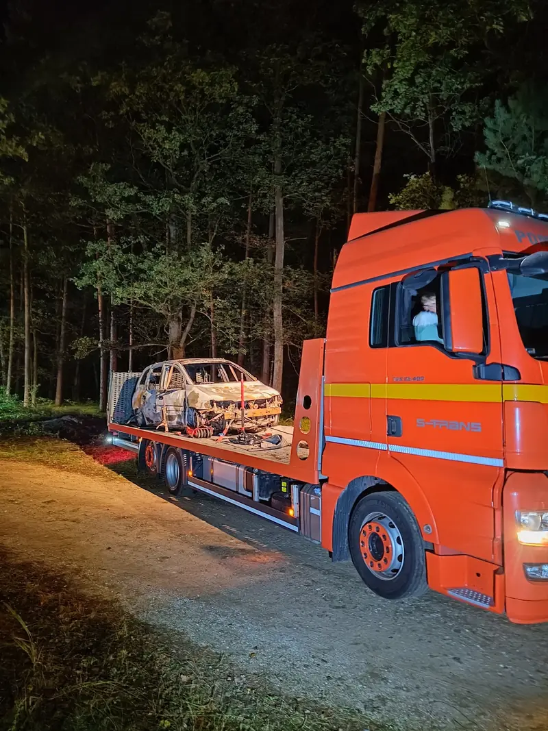 Laweta S-Trans z wrakiem spalonego samochodu na leśnej drodze nocą